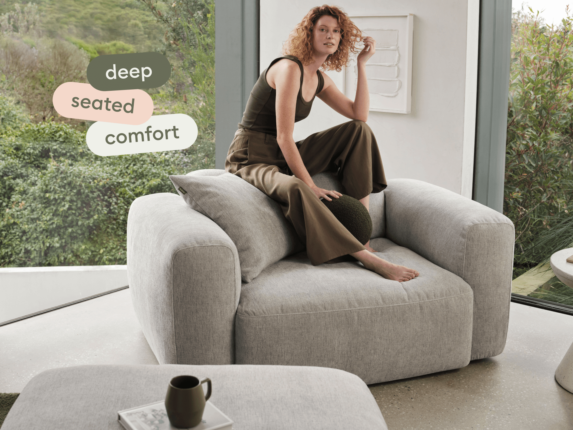 Luxurious grey upholstered armchair crafted from plush fabric, featuring deep seating and wide armrests. Positioned in a serene, nature-inspired living space.
