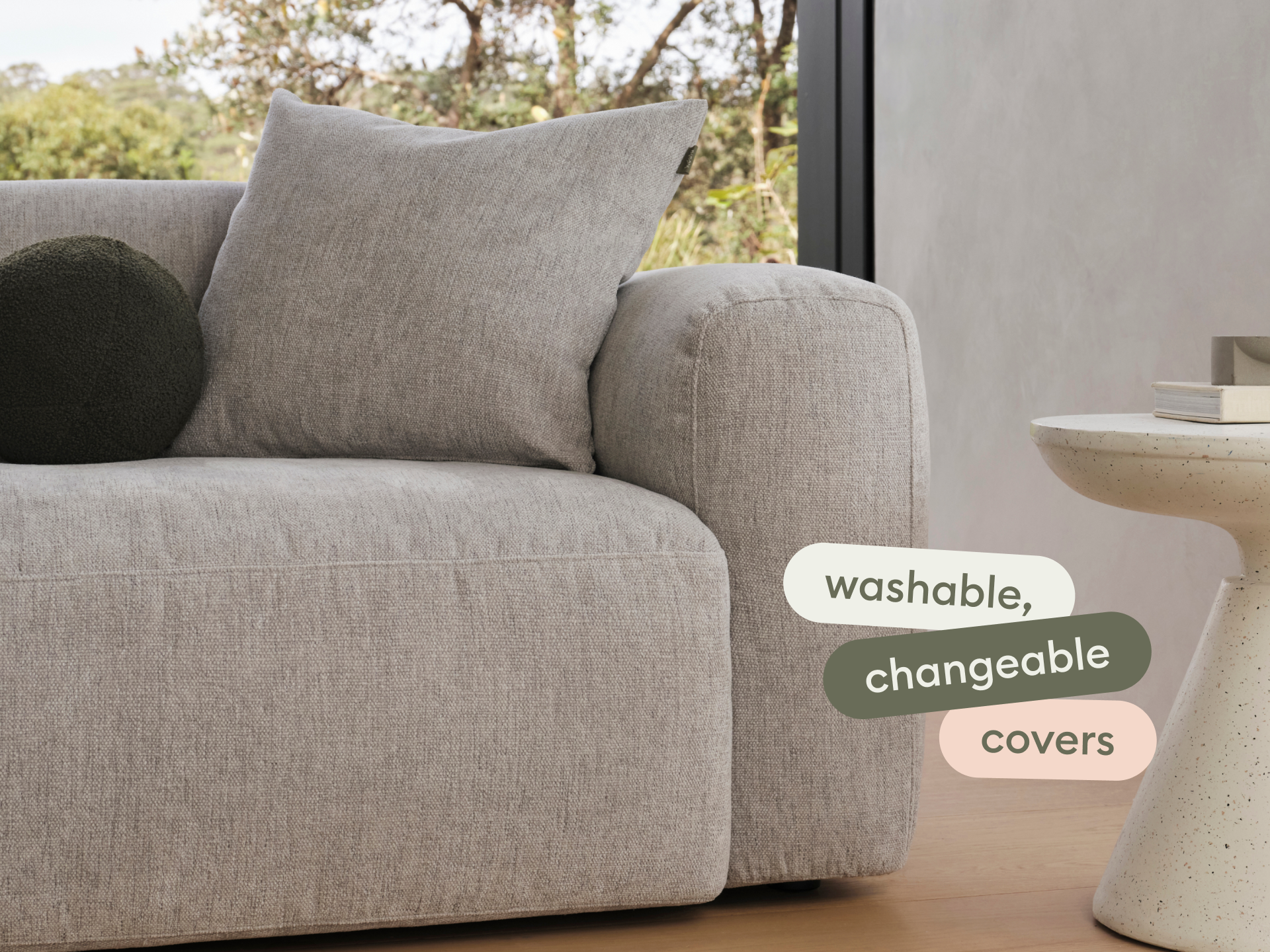 Modern grey linen sofa with plush, washable, changeable covers. Set in a minimalist living room with a sleek, white side table. Unobtrusive luxury.