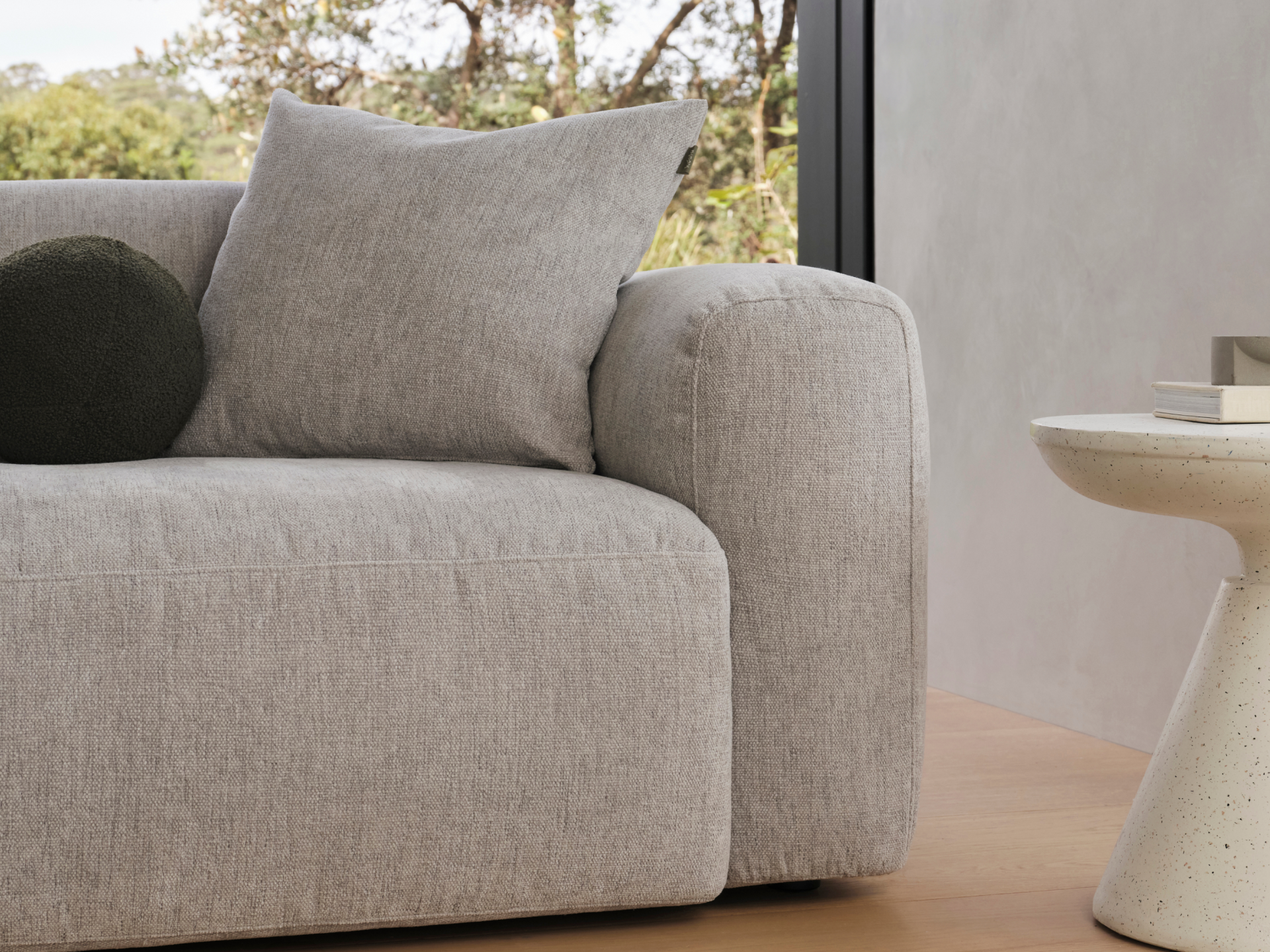 Luxurious grey fabric sofa with plush cushions, paired with a sleek cream marble side table in a minimalist, light-filled living room setting.