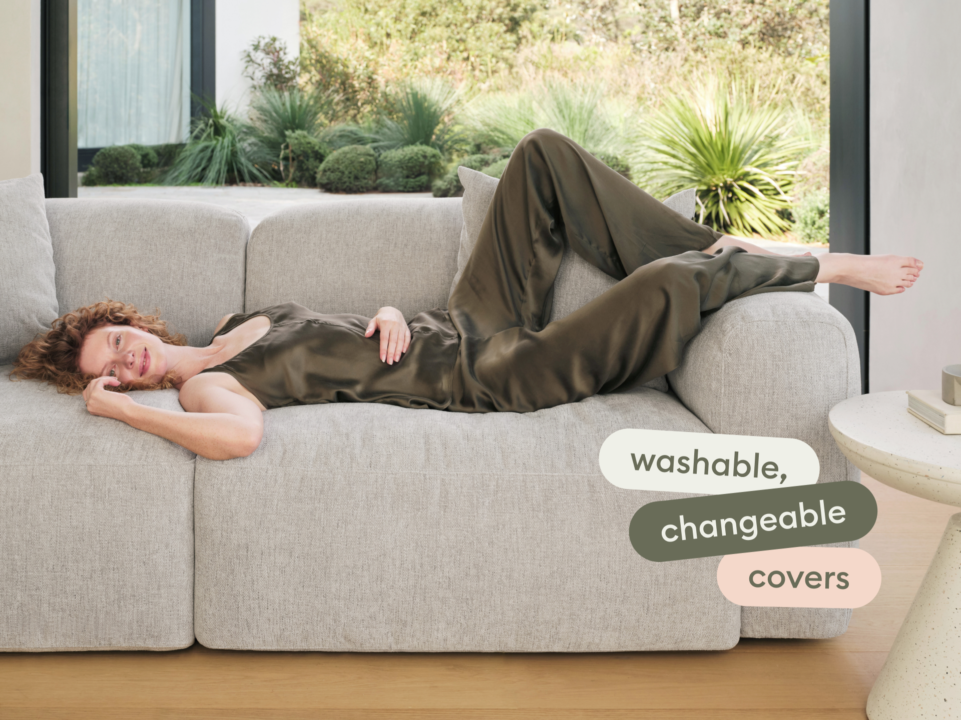 Luxurious grey upholstered sofa featuring washable, changeable covers. Set in a modern living space with light wood flooring and lush garden views.