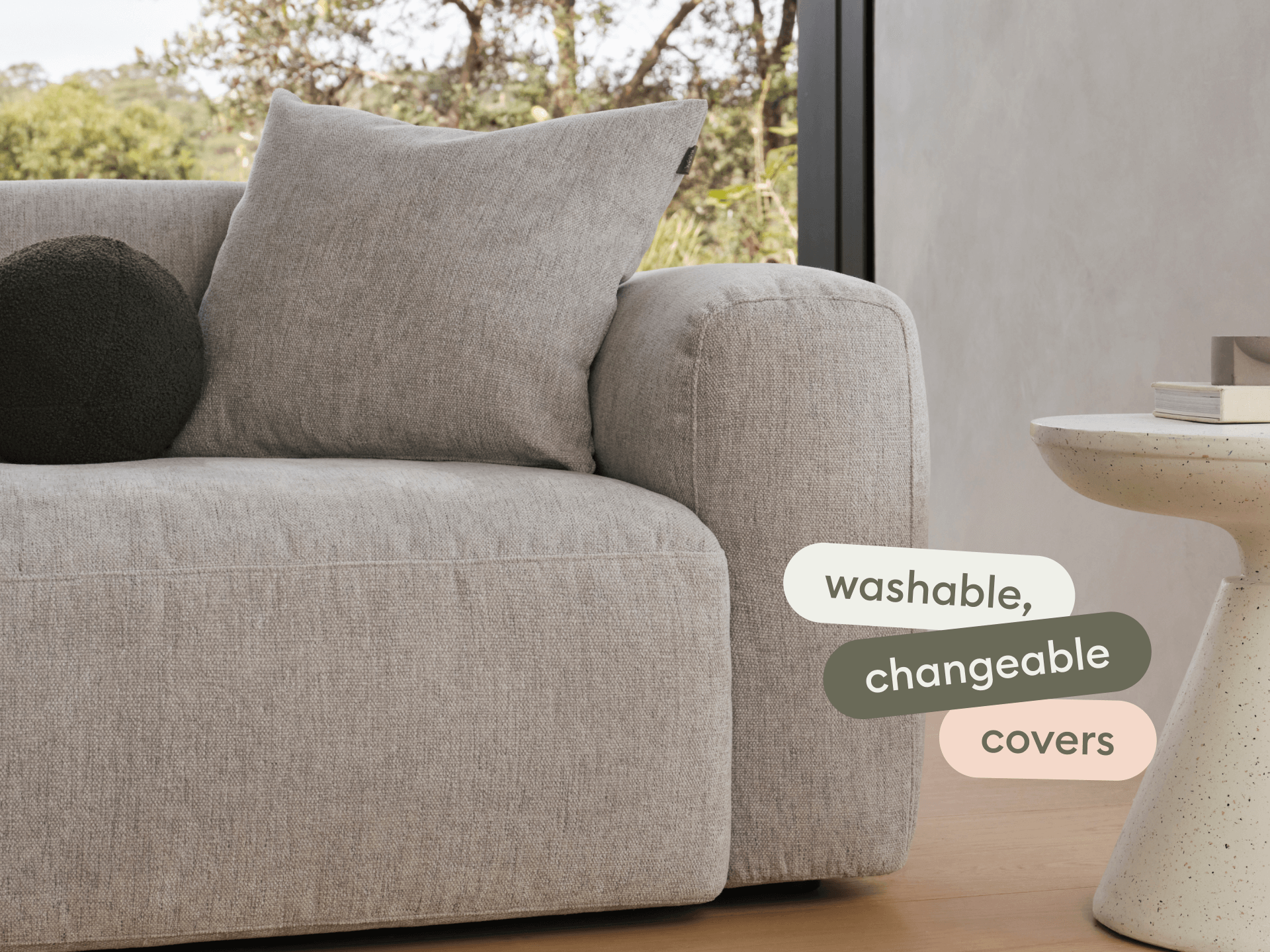 Luxurious grey fabric sofa with washable, changeable covers. Features plush cushions. Positioned in a modern living space with natural light.
