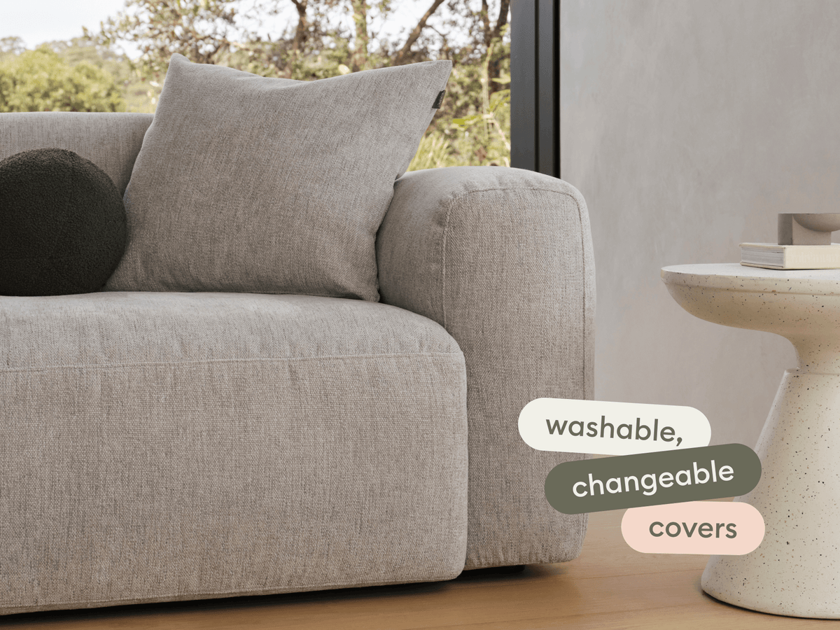 Modern grey linen sofa with plush cushions, featuring washable, changeable covers. Set beside a minimalist terrazzo side table in a sunlit living space.