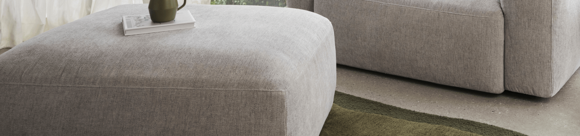 Luxurious grey fabric ottoman in a minimalist living room, featuring plush upholstery and sleek design, complemented by a stylish grey sofa.