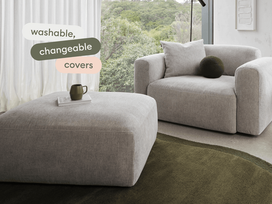 Luxury armchair and ottoman set in light grey fabric, showcasing washable and changeable covers. Features plush cushions, set on a minimalistic concrete floor.
