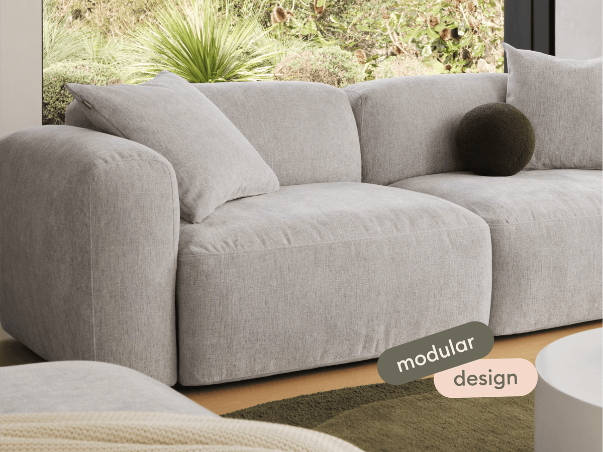 Elegant modular sofa in light grey linen, featuring plush cushions and rounded armrests. Set in a chic living room with a modern, minimalist aesthetic.