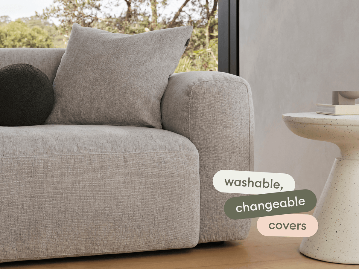 Luxurious grey linen sofa with soft, washable, changeable covers. Rounded edges, plush cushions. Paired with a sleek, textured white side table.