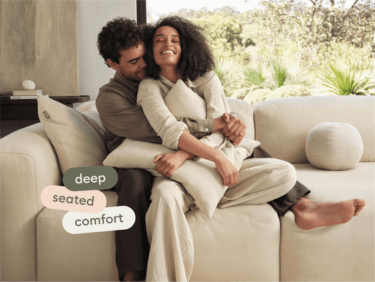 Luxurious beige sectional sofa with deep seating, plush fabric, and minimalist design, set in a serene living space overlooking lush greenery.