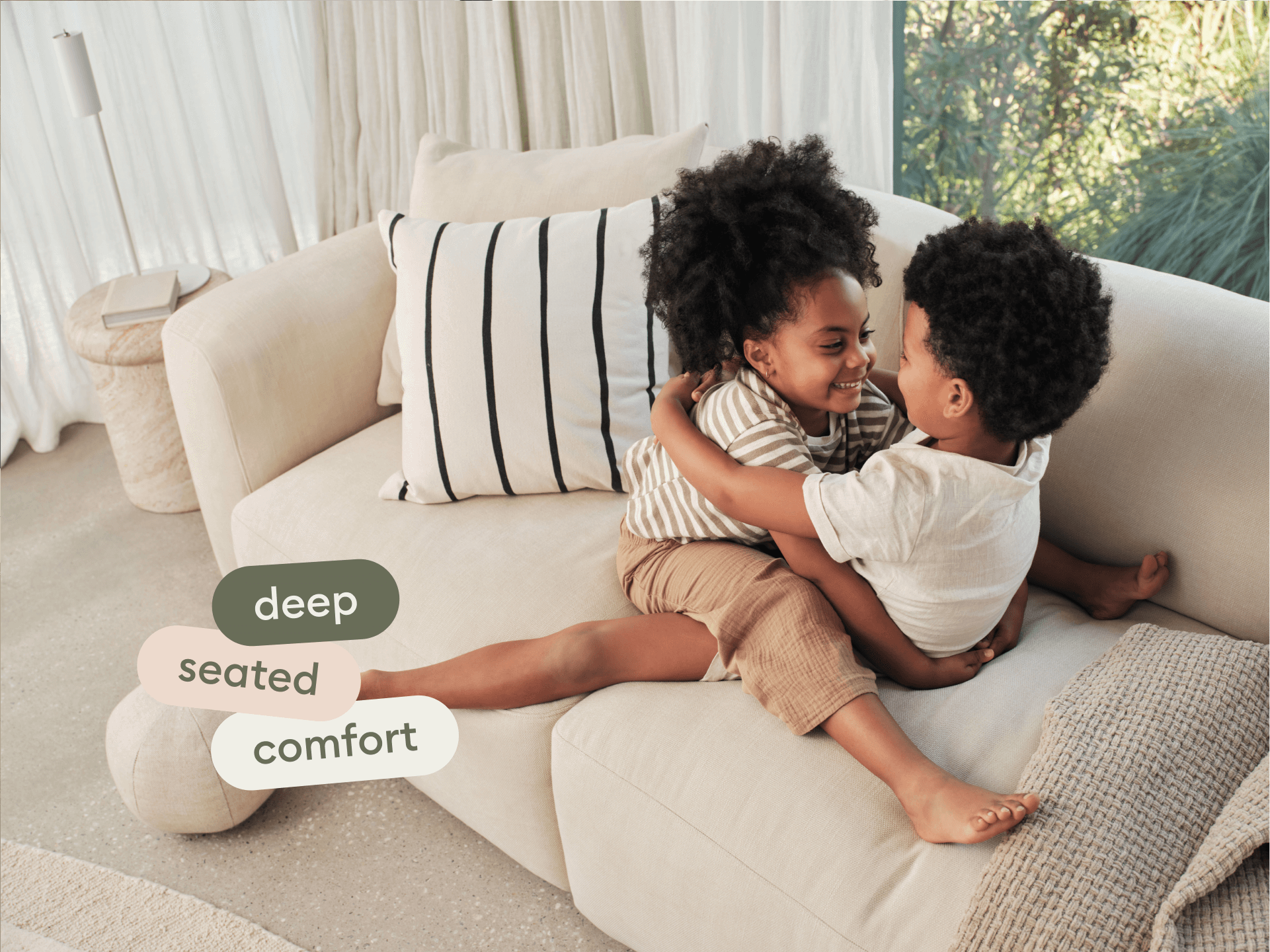 Modern beige sectional sofa with plush fabric upholstery, deep seating, and minimalist design. Set in a light, airy living room with sheer curtains.