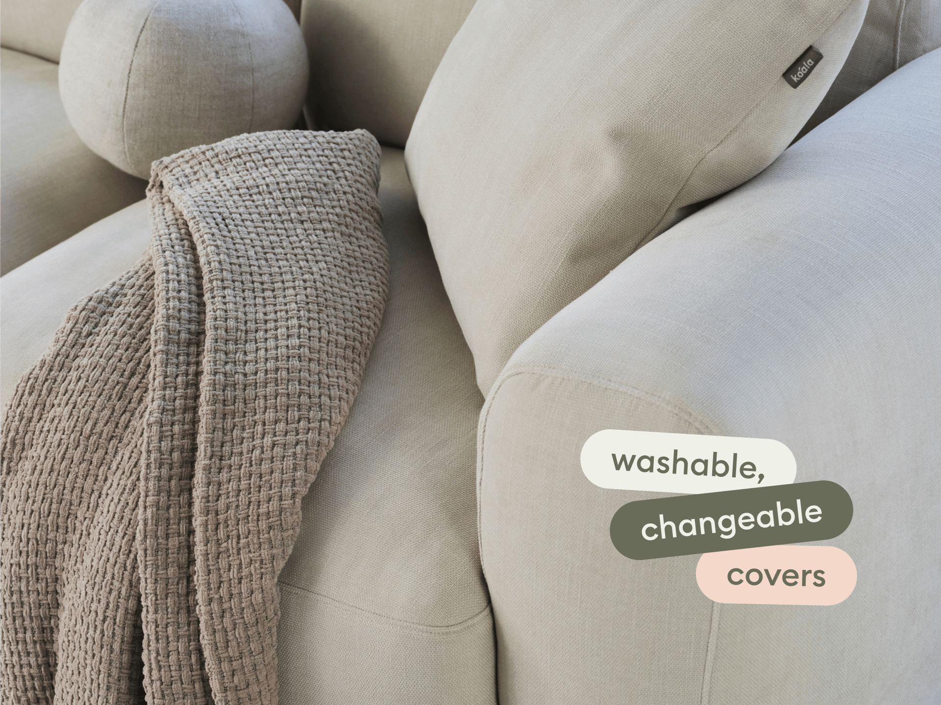 Premium beige linen sofa with plush cushions, featuring washable, changeable covers. Complemented by a textured taupe throw. Modern luxury setting.