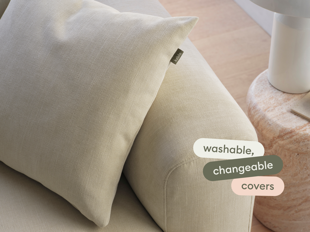 Beige linen sofa with washable, changeable covers, showcasing a minimalist, rounded armrest. Set beside a round, light stone side table.