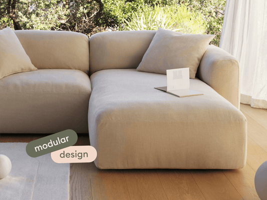 Luxurious beige modular sofa in premium linen, featuring deep-set cushions and a streamlined silhouette. Set in a sunlit living room with wooden floors.