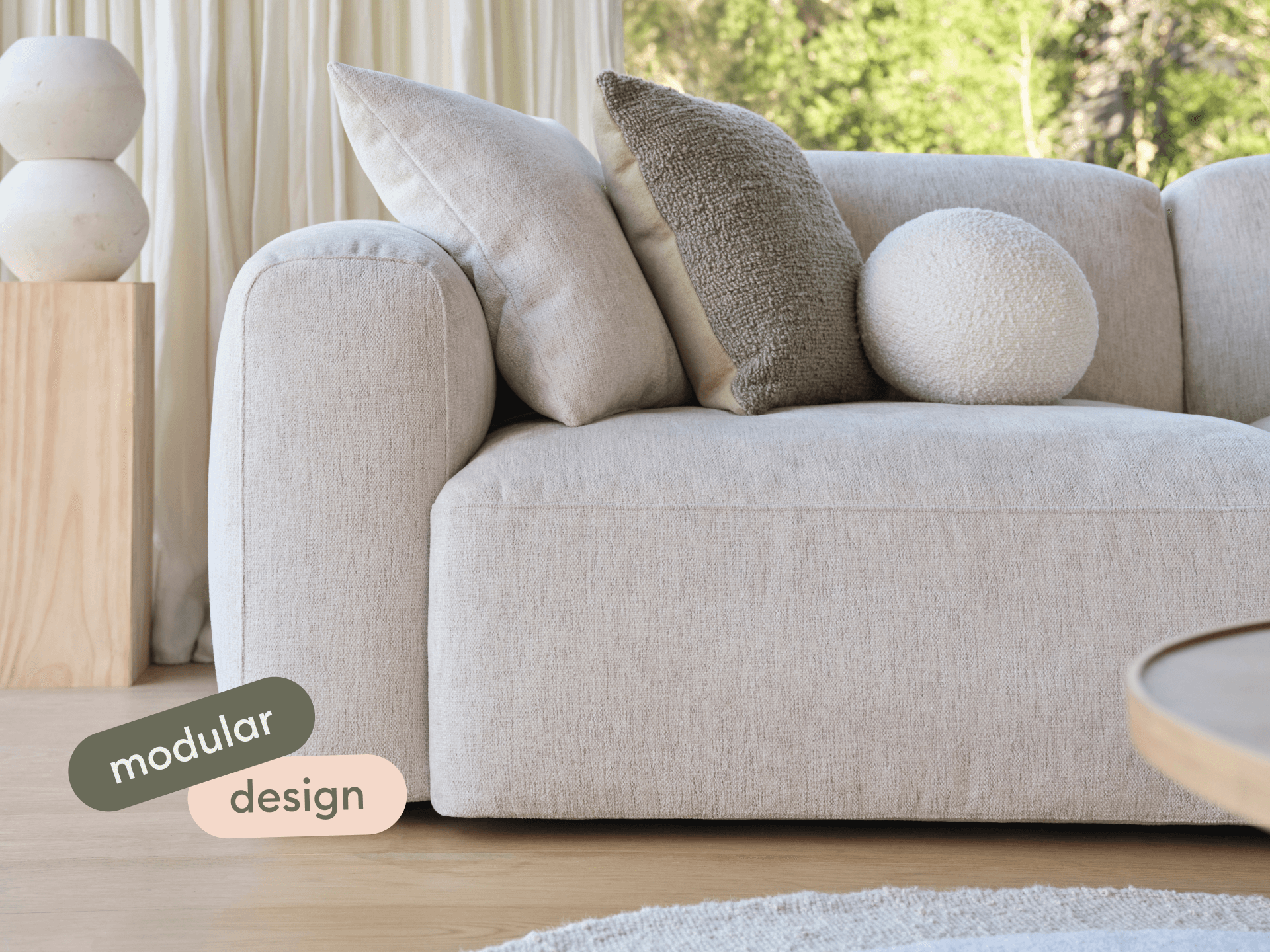 Luxurious modular sofa in cream fabric, featuring rounded edges and plush cushions. Set in an elegant living space with natural light and wooden accents.