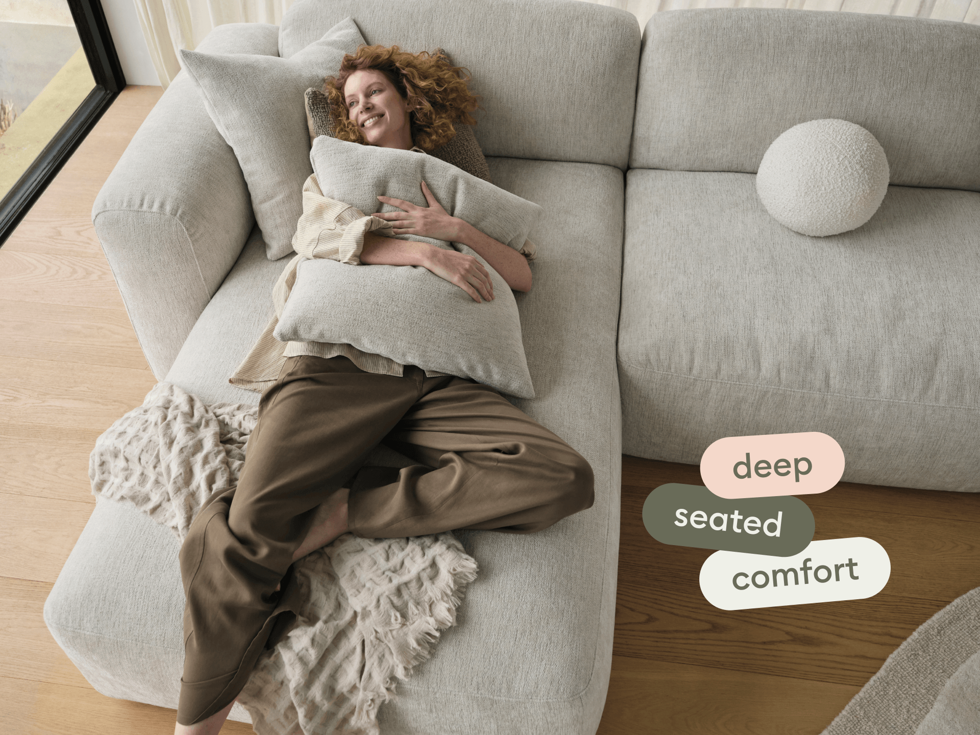 Luxurious beige sectional sofa in plush fabric, featuring deep seating, and minimalist design, set on light wooden flooring near expansive windows.