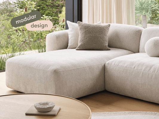 Luxurious modular sofa in soft beige fabric, featuring plush cushions and contemporary design. Set in a chic living room with large windows and natural light.
