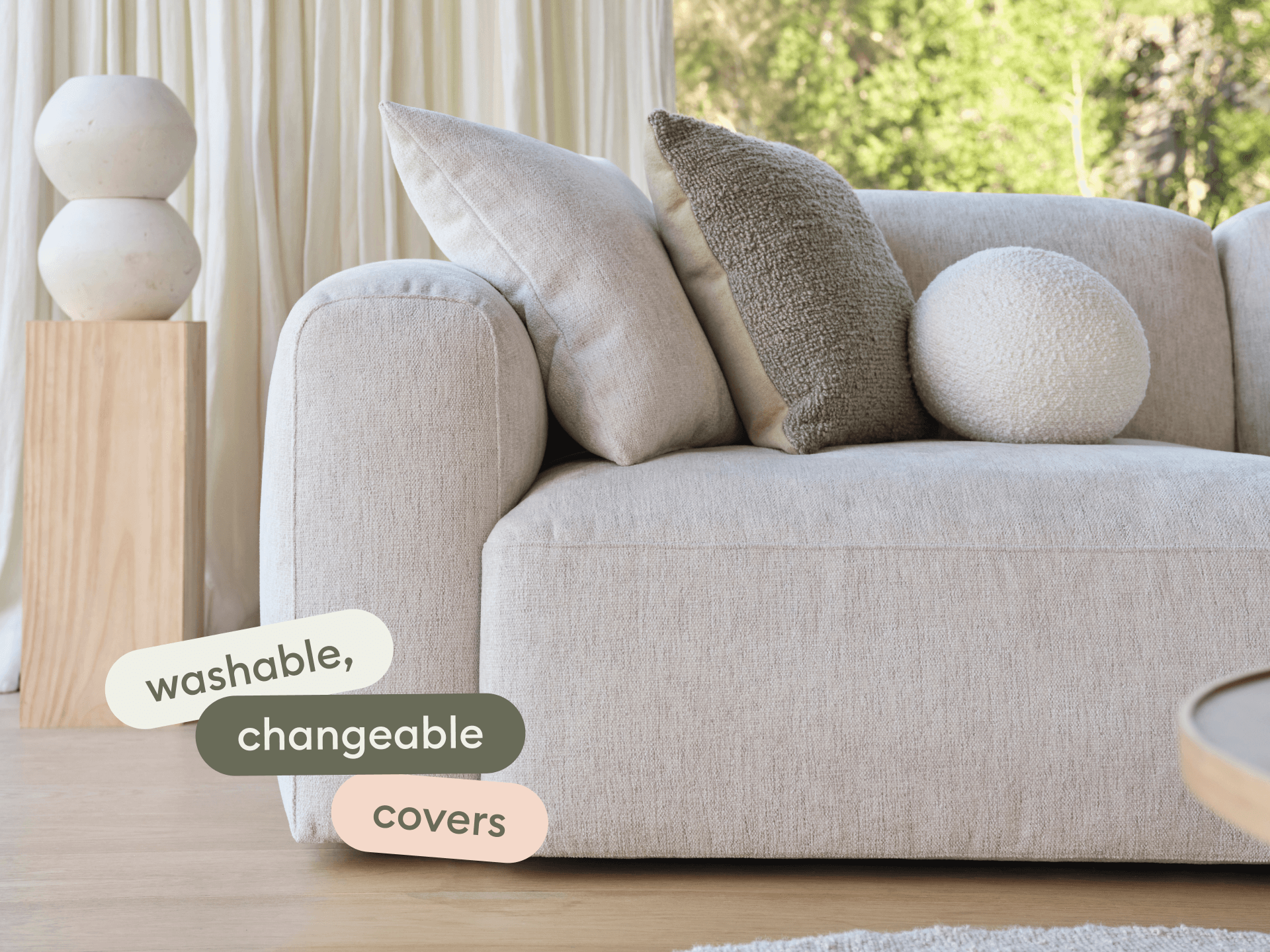 Luxurious beige fabric sofa with washable, changeable covers. Features plush cushions in a light-filled, modern living room with natural wood flooring.