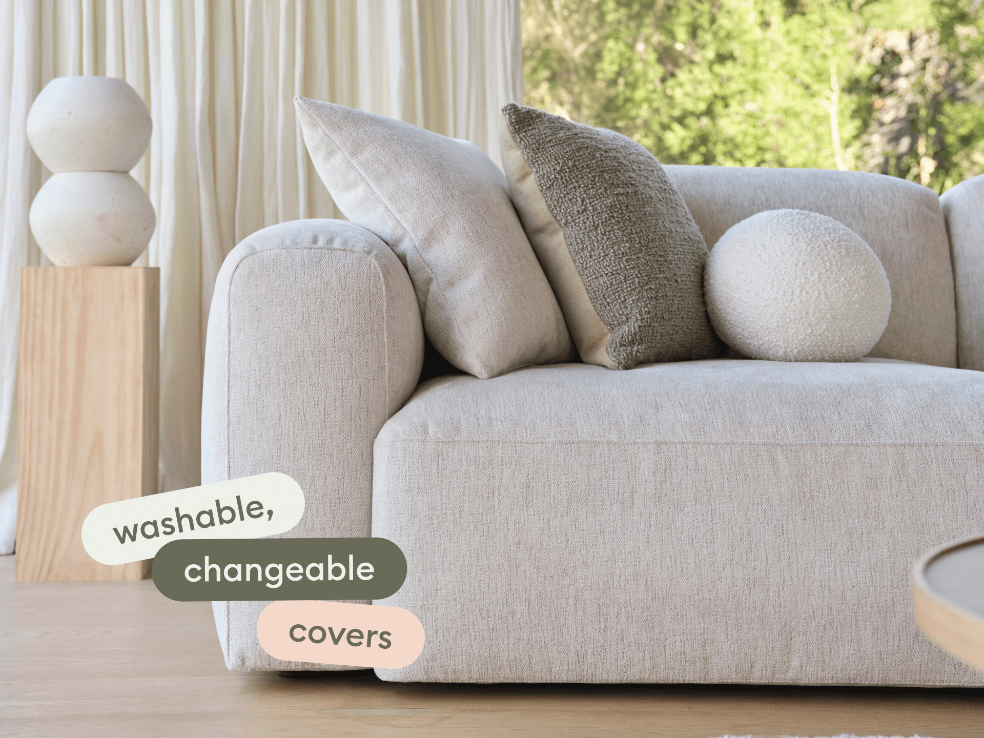 Luxurious cream linen sofa with plush, washable covers. Features rounded cushions and soft-textured pillows. Set in a sunlit, elegant living space.
