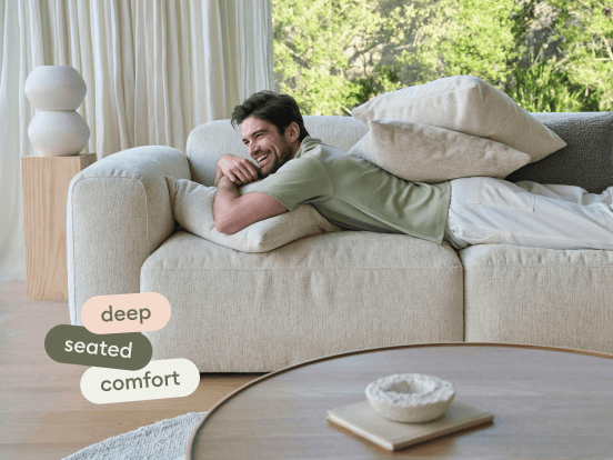 Luxurious beige linen sofa with deep seating, plush cushions, and a relaxed silhouette, set against airy curtains and a serene outdoor view.
