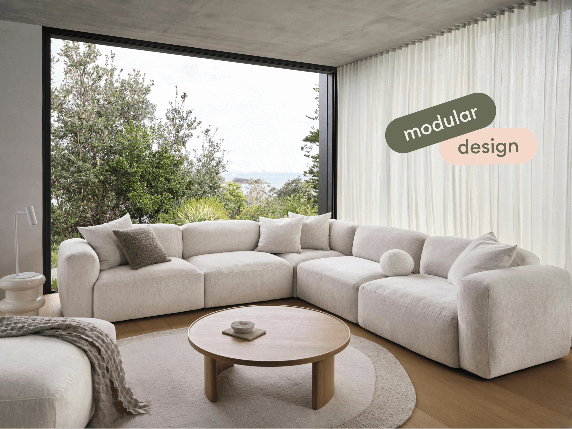 Luxurious modular sofa in plush cream fabric, featuring deep seats and plush cushions. Set in a sleek, modern living space with floor-to-ceiling windows.