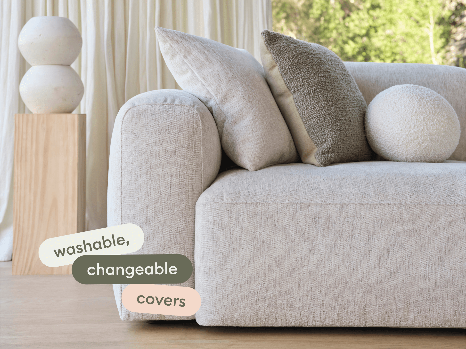 Modern beige fabric sofa with plush cushions, featuring washable and changeable covers. Set in a bright, airy room with wooden accents.