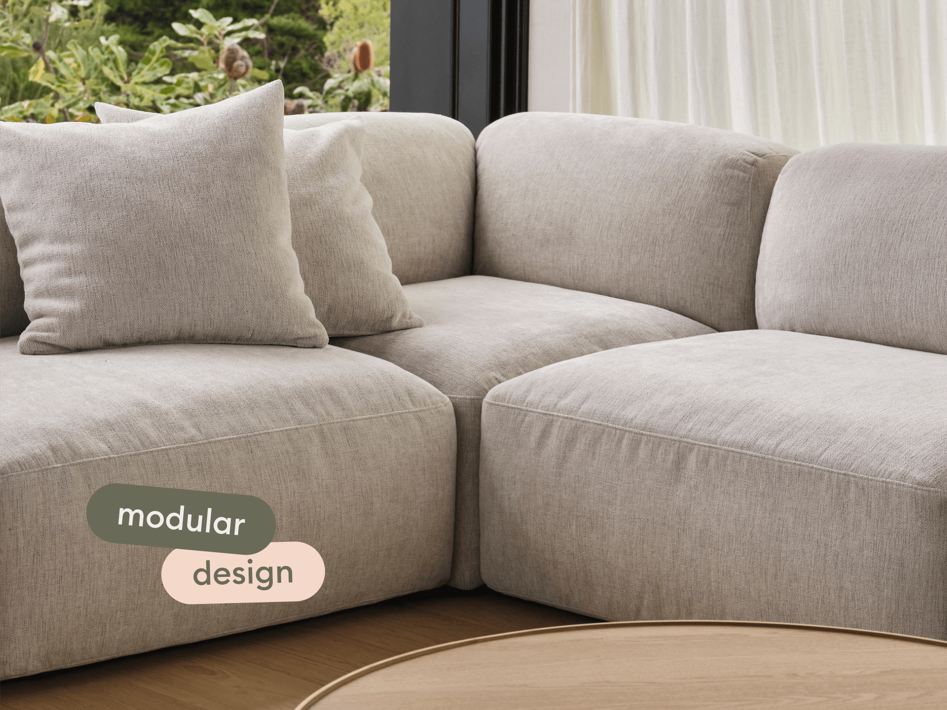 Premium modular sofa in soft beige fabric, featuring plush cushions and seamless stitching, set against a natural light-filled interior with a wooden floor.