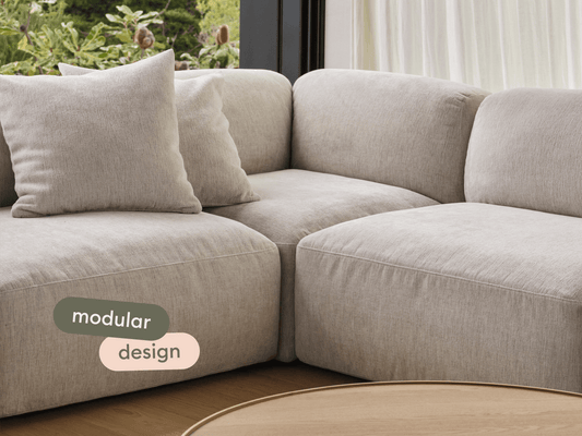 Premium modular sofa in soft beige fabric, featuring plush cushions and seamless stitching, set against a natural light-filled interior with a wooden floor.