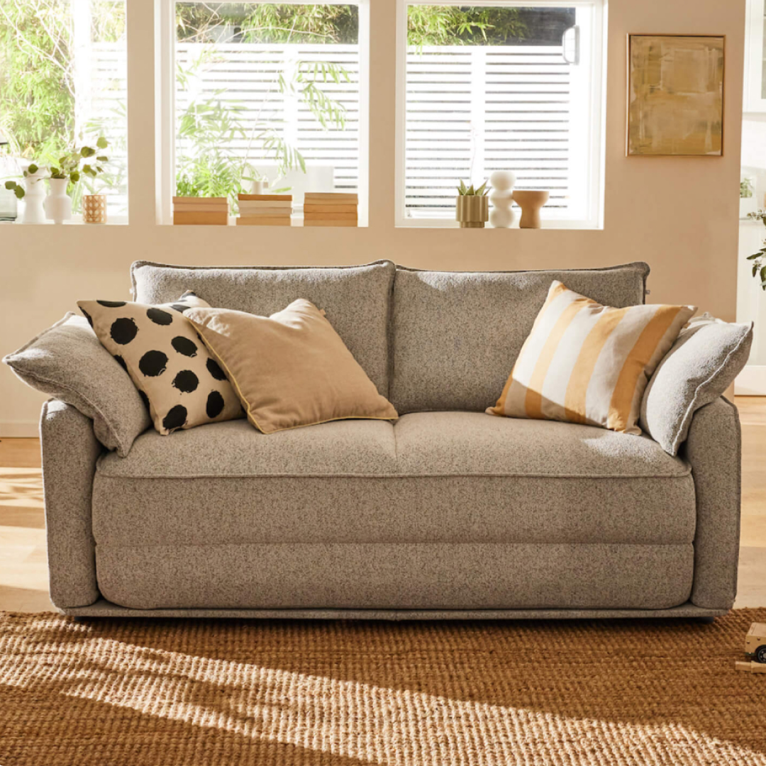A light grey sofa with plush cushions, featuring a black polka dot pillow and a gold-striped pillow, on a woven jute rug.