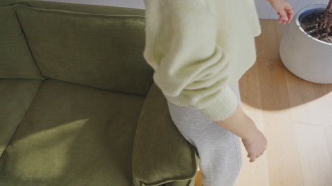 person falling back on comfortable olive green sofa in a modern living room